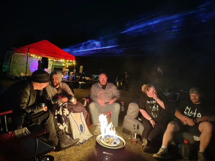 Guests gathered around a fire bowl beside the illuminated DJ canopy.