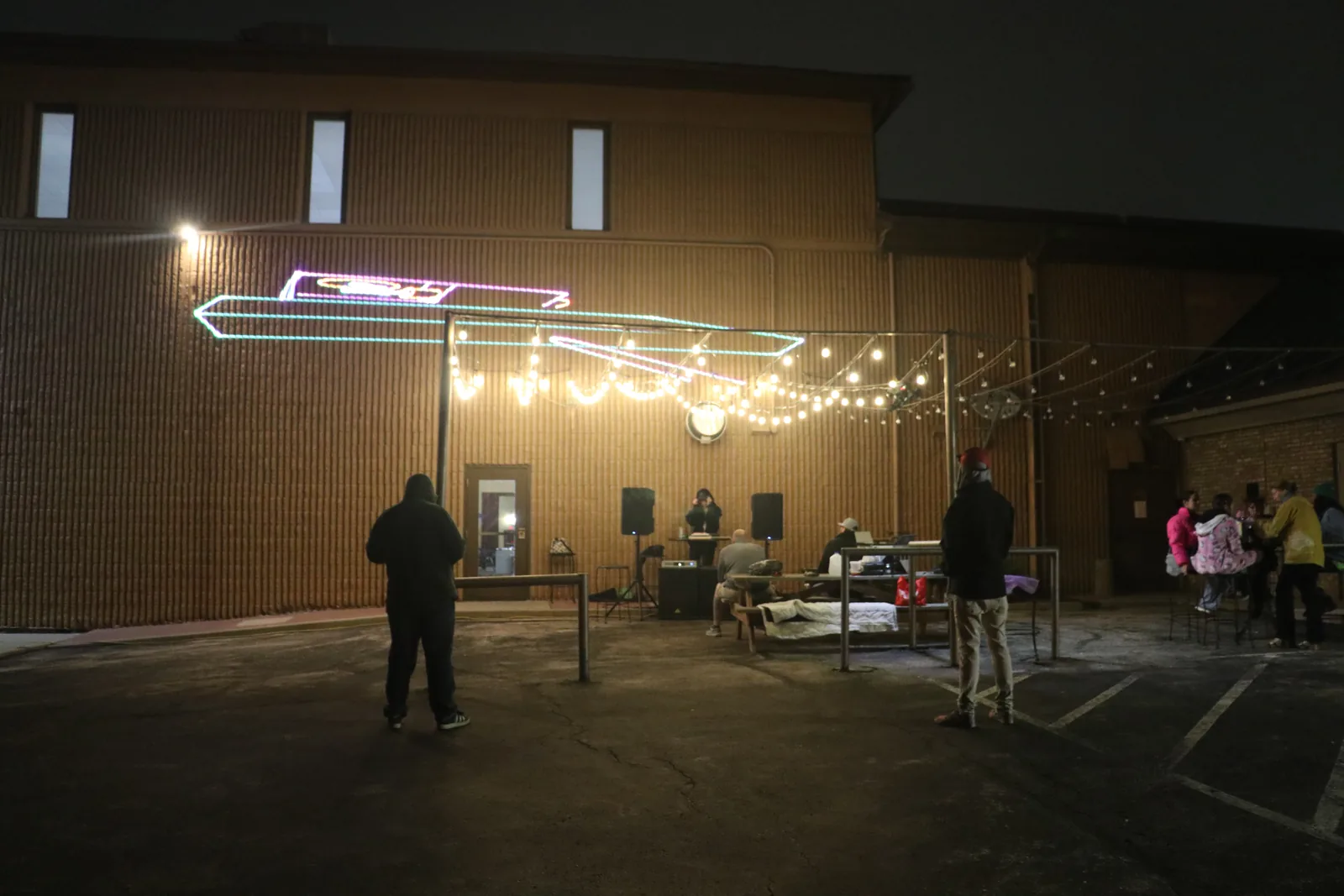 A courtyard DJ set beneath string lights and colorful wall projections.