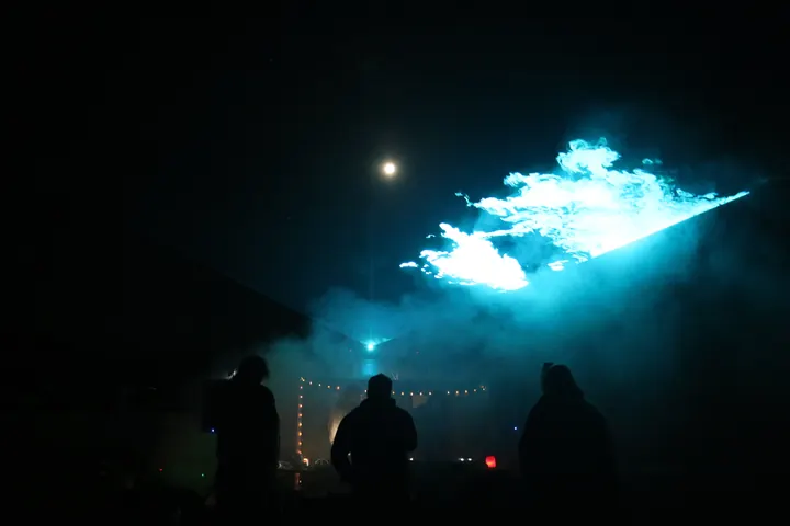 Three guests silhouetted beneath cyan lasers and illuminated haze.