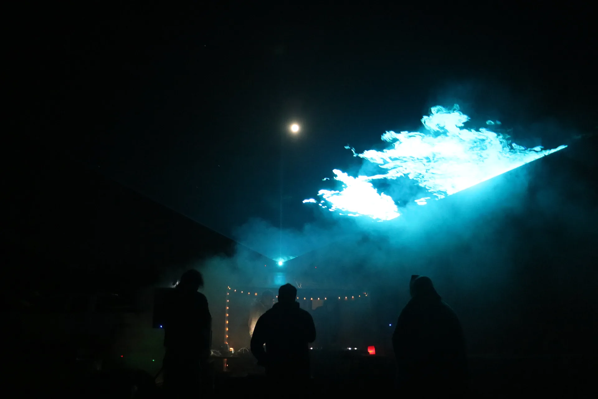 Three guests silhouetted beneath cyan lasers and illuminated haze.