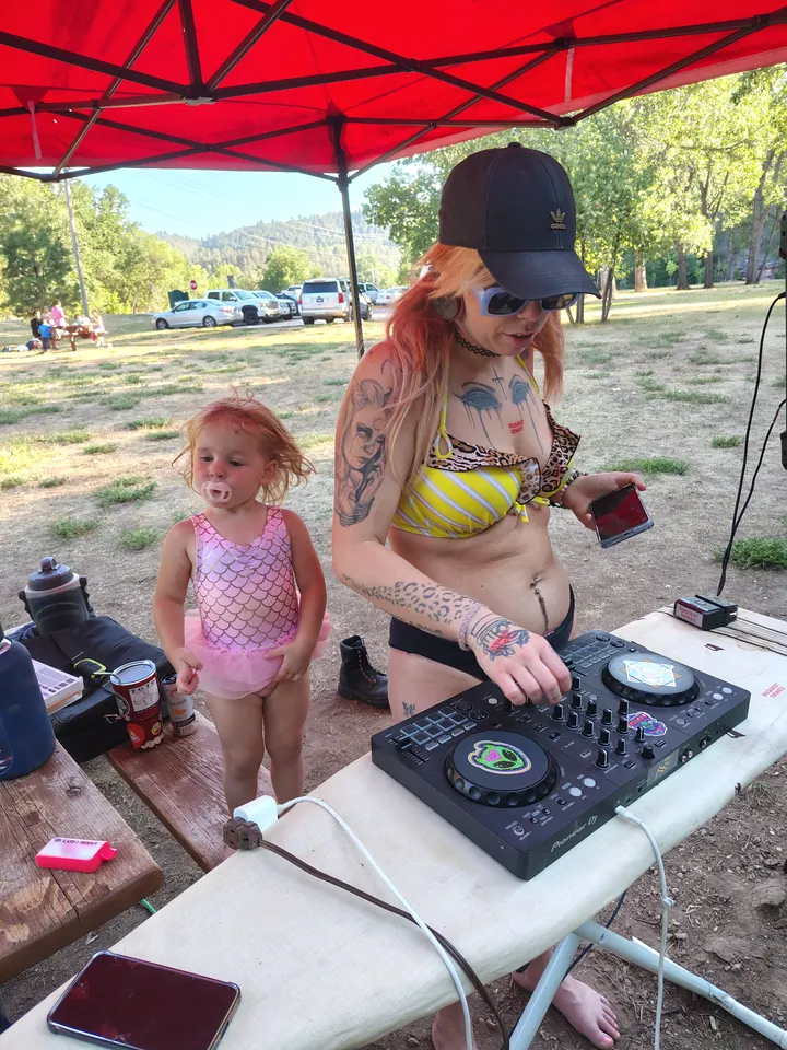 A DJ working under a red canopy, with a child beside the table.