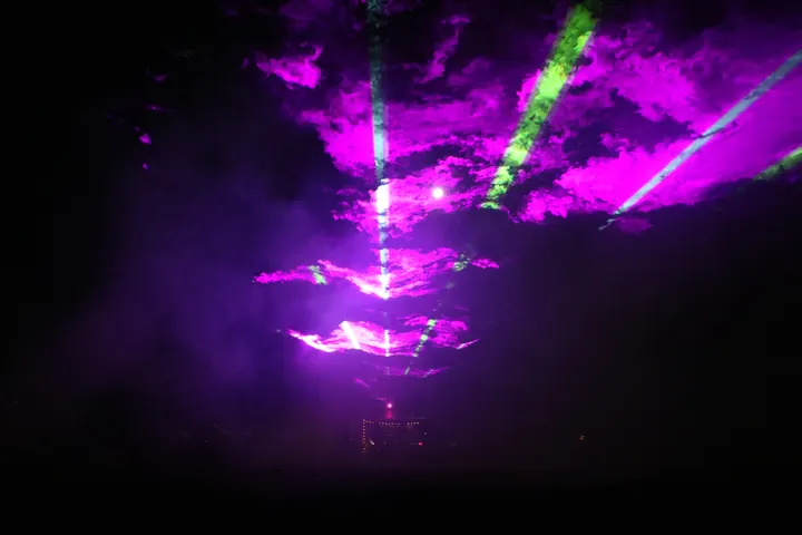 Purple and green lasers cutting through haze above the outdoor setup.